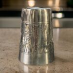 A beautifully handcrafted 7-inch WellnessCarve Bronze Glass with intricate carvings and a smooth finish, showcased elegantly in a rustic setting