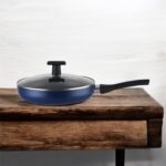 Blue non-stick induction fry pan with glass lid and long handle, shown on a modern kitchen counter; suitable for gas and induction stoves.