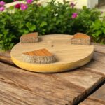 A round hardboard chakla with a dark brown top surface and yellow edges, featuring three anti-slip base supports, placed on a rustic wooden surface.