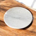 A round, natural white marble roti chakla with a smooth finish, perfect for rolling rotis and puris while adding an elegant touch to any kitchen.