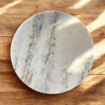 A white marble chakla with a smooth finish and anti-slip rubber base, ideal for rolling rotis and puris on any kitchen surface.