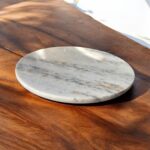 A white marble chakla with a smooth finish and anti-slip rubber base, ideal for rolling rotis and puris on any kitchen surface.