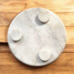 A white marble chakla with a smooth finish and anti-slip rubber base, ideal for rolling rotis and puris on any kitchen surface.