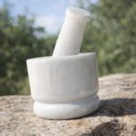 Solid white marble mortar and pestle set (4 inch khal batta) used for grinding spices, herbs, and Ayurvedic ingredients in a traditional kitchen setting.