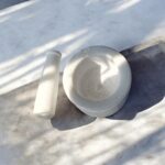 Solid white marble mortar and pestle set (4 inch khal batta) used for grinding spices, herbs, and Ayurvedic ingredients in a traditional kitchen setting.